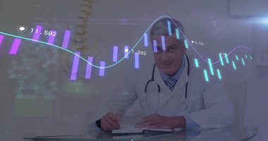 Writing doctor scribbling on notepad at clinic desk with stethoscope showing spine model and graphs. Medical, healthcare, analysis, technology, innovation, professionalism, diagnostics