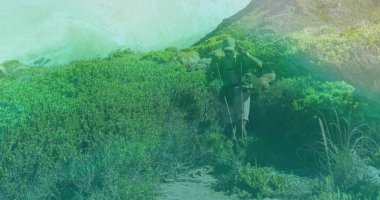 Walking hiker wearing green cap and jacket on coastal trail, with trekking poles and small backpack. Adventure, exploration, outdoor, rugged, nature, health, activity