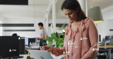 Monitoring overlaid metrics on laptop, mid-adult woman of color at desk in open office, copy space. Collaboration, productivity, digital, workspace, modern, technology, teamwork