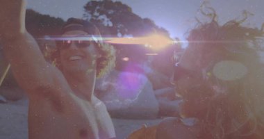 Laughing friends dancing on shoreline at beach sunset, with baseball cap and sunglasses. Joy, leisure, outdoor, vibrant, celebration, companionship, vacation