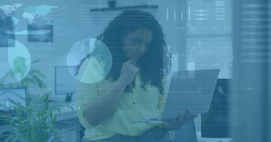 Sitting woman wearing work attire holding laptop and resting chin in office with monitors, plants. Professional, workspace, contemporary, technology, collaboration, productivity, minimalist
