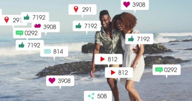 Walking romantic couple in casual summer clothes on sandy shore, with floating social media icons. Romance, leisure, seaside, happiness, lifestyle, communication, vibrancy