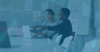 Women in business attire pointing at silver laptop in conference room, with printed charts. Corporate, teamwork, presentation, consultation, professional, modern, productivity