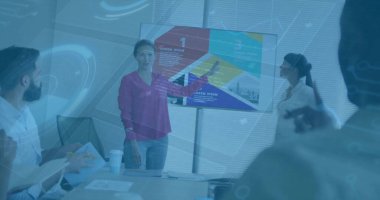 Pointing presenter wearing magenta blouse leading meeting in room at conference table, with monitor. Collaboration, teamwork, digital interface, corporate, professional, presentation, brainstorming