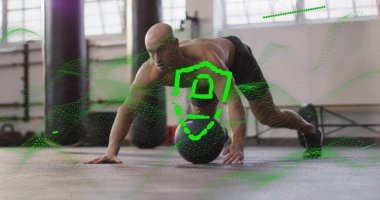 Balancing muscular bald man in black shorts on weighted medicine ball in studio, with weight plates. Strength training, fitness, workout, gym environment, functional exercise, athletic, strength