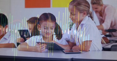 Working two girls wearing polos using tablets in classroom, with smartphone, posters and bar charts. Education, collaboration, digital learning, classroom, technology, youth, teaching
