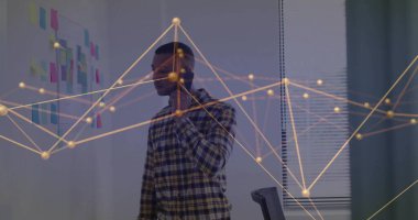 Standing African American man speaking into smartphone in office with sticky notes and data overlay. Collaboration, innovation, communication, teamwork, technology, productivity, strategy