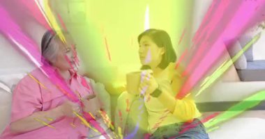 Anne ve kızı kanepede oturuyor, saniyeler sonra gökkuşağı ışınları pazarlamayı parlaklaştırıyor. Aile, bağ, rahatlama, uyum, canlı, rahat, sevgi