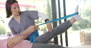 Sağlık terapisti hasta ayağına mavi bant takıyor ve bacak kaldırma hareketini derinleştiriyor. Rehabilitasyon, fizyoterapi, egzersiz, hareketlilik, sağIık, klinik, aktif