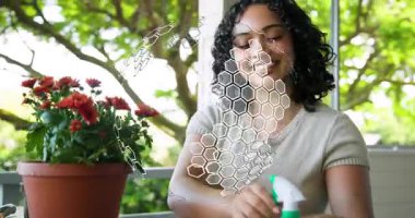 Bahçıvan bahçe işlerinde verandada yeşil sprey şişesine uzanıyor, sisliyor ve kırmızı çiçekleri buduyor. Bahçecilik, çiçek bakımı, açık havada yaşam, botanik, dinginlik, çevre dostu, sağlık.