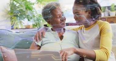 Anne ve kızı kanepede oturuyor, kızı yarış pistini tıkırdatıyor ve dijital tarama becerileri öğretiyor. Aile, akıl hocalığı, bakım, nesiller arası, teknoloji, konfor, ev