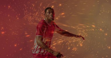 Twisting athlete wearing red jersey and shorts in studio, with orange gold particles, copy space. Movement, energy, vitality, athleticism, dynamism, performance, sport