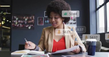 Pazarlamacı masa başında tasarımları sınıflandırıyor, sayfaları çeviriyor ve nişan tezgahlarını etkinleştiriyor rehber notlar. Yaratıcılık, dijital pazarlama, profesyonel, modern, üretkenlik, iletişim, analiz