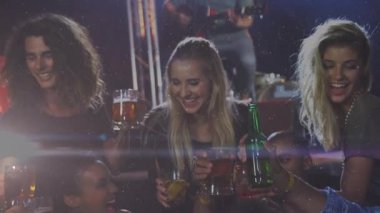 Arkadaşlar bira bardaklarını kaldırıyor ve kırmızı-mavi ışık altında bar tostuna tezahürat yapmak için yeşil şişeyi eğiyorlar. Kutlama, yoldaşlık, gece hayatı, sosyalleşme, eğlence, sıcak aydınlatma, şenlik