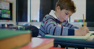 Çizgili süveter giyen bir öğrenci. Okul masasında kitap yığınıyla kalem kullanıyor. Kopya alanı. Eğitim, öğrenim, odaklanma, konsantrasyon, akademik, sınıf, öğrenim