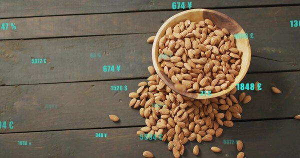 Показаны деревянные чаши, проливающие миндаль на деревянный стол, плавающие бирюзовые валютные аннотации. Закуски, финансовые, цифровые, ржавые, органические, накладываемые, случайные