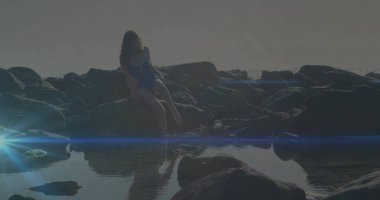 Sahilde kayalara tüneyen benekli mayo giyen ışıl ışıl mercek ve gelgit havuzlu güzel bir kadın. Araştırma, macera, eğlence, dinginlik, doğa, yansıma, açık hava