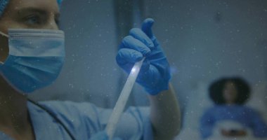 Hastane odasında mavi önlüklü, maskeli ve eldivenli bir hemşire hasta yatağının yanında şişe tutuyor. Tıbbi, klinik, laboratuvar, araştırma, sağlık, teşhis, kesinlik