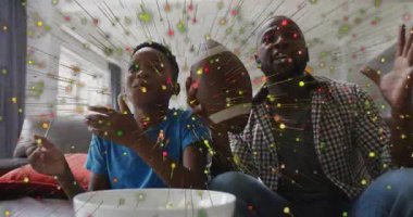 Father and son reacting to confetti and celebrating football win on couch, showcasing technology. Family, celebration, joy, companionship, digital effects, leisure, warmth