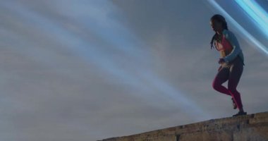 Koşucu çatı çıkıntısında yüksek diz matkabını çalıştırıyor. Mavi ışık çizgisi formda olduğunu gösteriyor. Atletizm, egzersiz, kararlılık, hareket, kentsel, enerjik, motivasyon