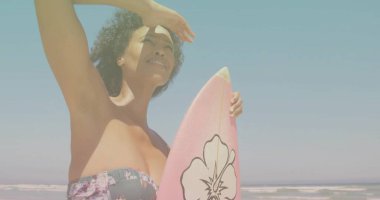 Shielding surfer in floral swimsuit holding pink surfboard at beach shore, with hibiscus design. Adventure, relaxation, coastal, vibrant, outdoor, leisure, lifestyle
