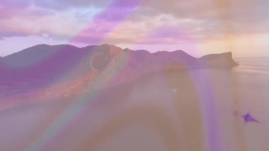 Opening shot spawning rainbow beams drifting across rocky coastal ridge, revealing sunset shadows. Ambient, ethereal, vibrant, luminous, surreal, tranquil, landscape