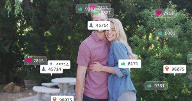 Bahçe avlusunda dijital konuşma baloncuklarıyla sıcacık kucaklaşan sıradan giyinmiş çift. Romantik, yakınlık, uyum, dinginlik, doğa, bağlantı, açık hava