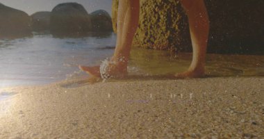 Sahilde gün batımında çıplak ayakla kayalık kayalarla ıslak kumda süzülen yürüyen bir erkek. Deniz manzarası, rahatlama, sükunet, doğal, açık hava, günbatımı, huzur.