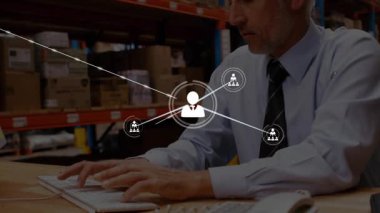 Man typing at logistics desk, profile icons generating network overlaying man and shelves. Technology, connectivity, data, digital, enterprise, professional, infrastructure