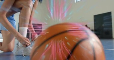 Spor salonunda spor ayakkabı bağı bağlayan diz çökmüş sporcu ayakkabı ve topun devre veri analizini etkinleştiriyor. Sporcu, performans, teknoloji, spor, takım çalışması, yenilik, enerji