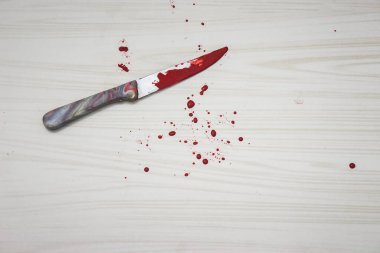 Yerde kanlı bir bıçak var. Bıçak suç mahallinde bulundu. Bir adli tıp, bıçaktan kan örnekleri alıyor. Arka planda seramik fayansların üzerinde kanlı bıçak var. Aile içi cinayet kavramı.