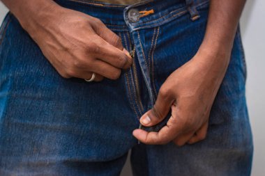 Fermuarlı kot pantolonun fermuarını açmaya çalışan ya da pantolonunun fermuarını elinde açan adam.