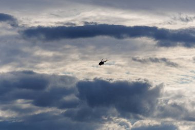Bir devriye görevi sırasında karanlık ve bulutlu bir gökyüzünde uçan askeri bir helikopter. Dramatik bulutlar ve siluet gergin ve güçlü bir atmosfer yaratır. Havadaki gücü, güvenliği ve hareketi simgeler.