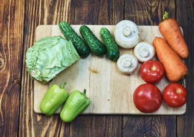 Kesme tahtasında sebzeler ve ahşap masa üstü manzarası, havuç, tatlı yeşil biber, domates, salatalık, mantar şampiyonları, yarım lahana lahana, sağlıklı yemek, beslenme