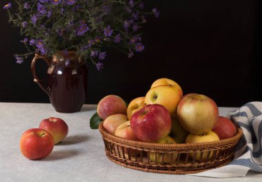 Elmalar dekoratif sepetin içinde siyah bir arkaplanda vazo ile 