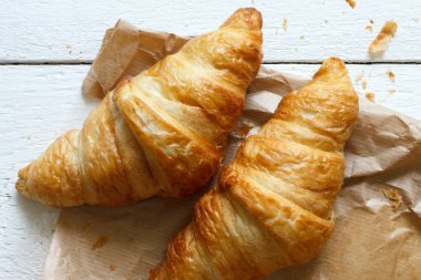 Kahverengi çantada kruvasanlar yukarıdan beyaz ahşap üzerinde.