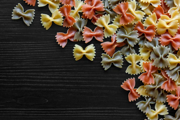 Droge gekleurde farfalle pasta op zwart getextureerd hout van bovenaf. S — Stockfoto