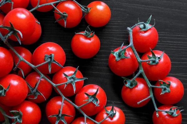 Small red tomatoes on the vine on black wood from above. — Stock Photo, Image