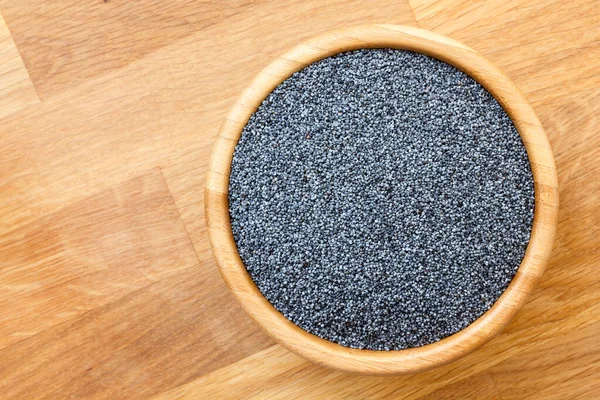 Poppy seeds in wood bowl on wood surface, from above, space for — Stock Photo, Image