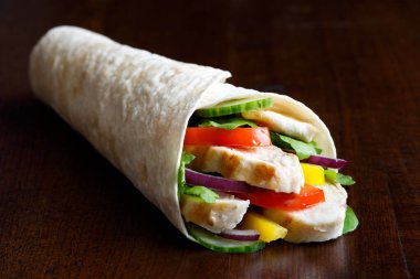 Izgara tavuk ve salatalı tortilla dürümü koyu bir sırt deliğinde izole edilmiş.