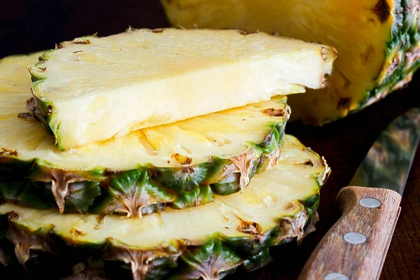 Whole pineapple cut up with pieces and knife on dark wood. — Stock Photo, Image