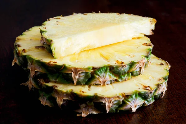 Ronde ananasschijfjes met geïsoleerde huid op donker hout. — Stockfoto