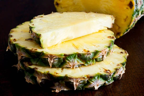 Whole pineapple cut up with pieces on dark wood. — Stock Photo, Image