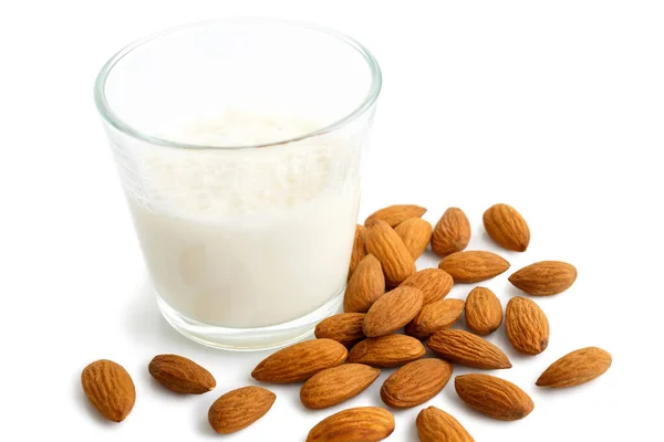 Pile of whole almonds next to glass of almond milk on white. — Stock Photo, Image