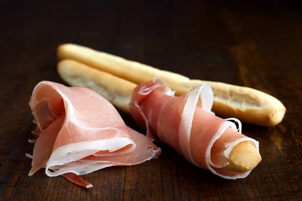 Jambon de prosciutto et bâtonnets de pain grissini. Isolé sur bois foncé . — Photo