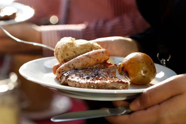 Hand hält einen Teller mit gegrilltem Fleisch, Wurst und Gemüse. — Stockfoto