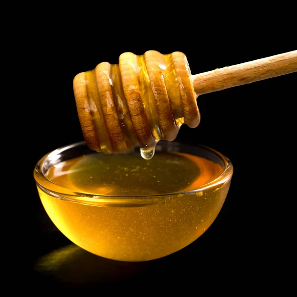 Wooden honey dipper over glass dish of honey. Black background. — Stock Photo, Image