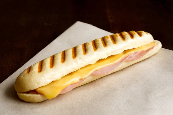 Cheese and ham toasted panini. On brown paper and wood. — Stock Photo, Image