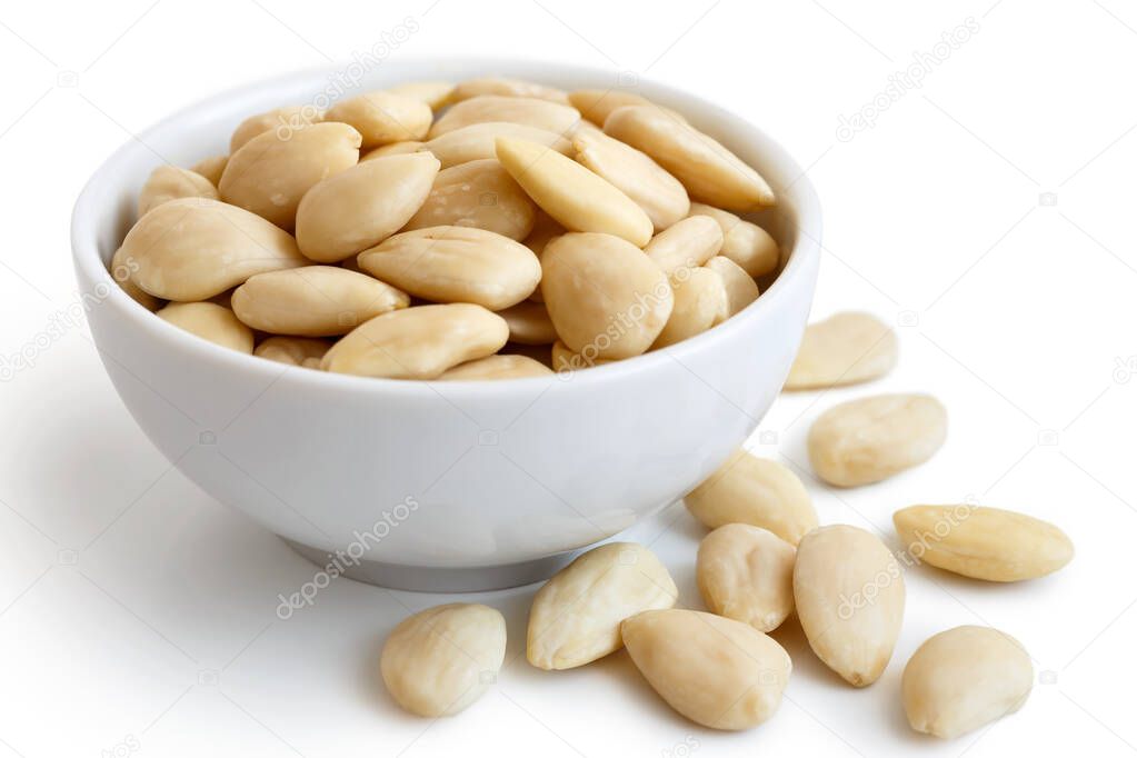 White bowl of peeled whole almonds on white. Spilled almonds.