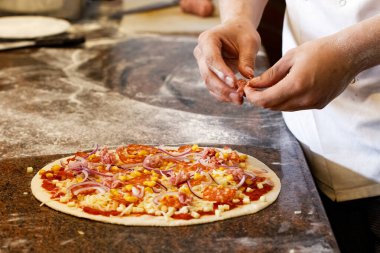 Aşçının elleri domatesli pizzaya salsiccia sosisi koyuyor..